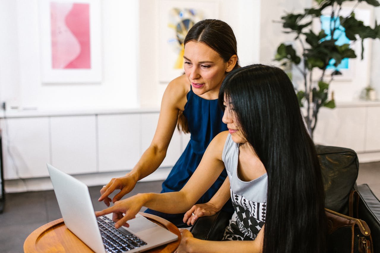 Two businesswomen discuss work on a laptop indoors. They look engaged and productive.
